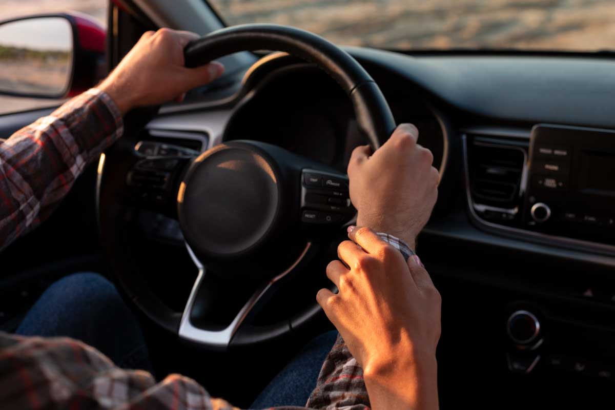 Hombre en vehículo con sus manos puestas en el volante.